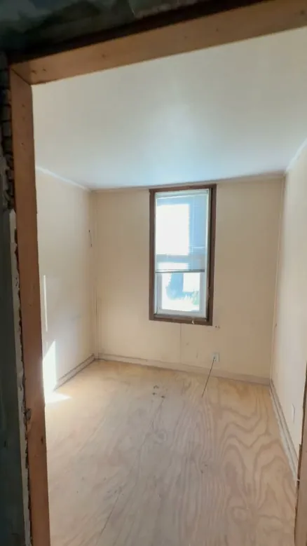 Empty room with a bare plywood floor after a cleanout